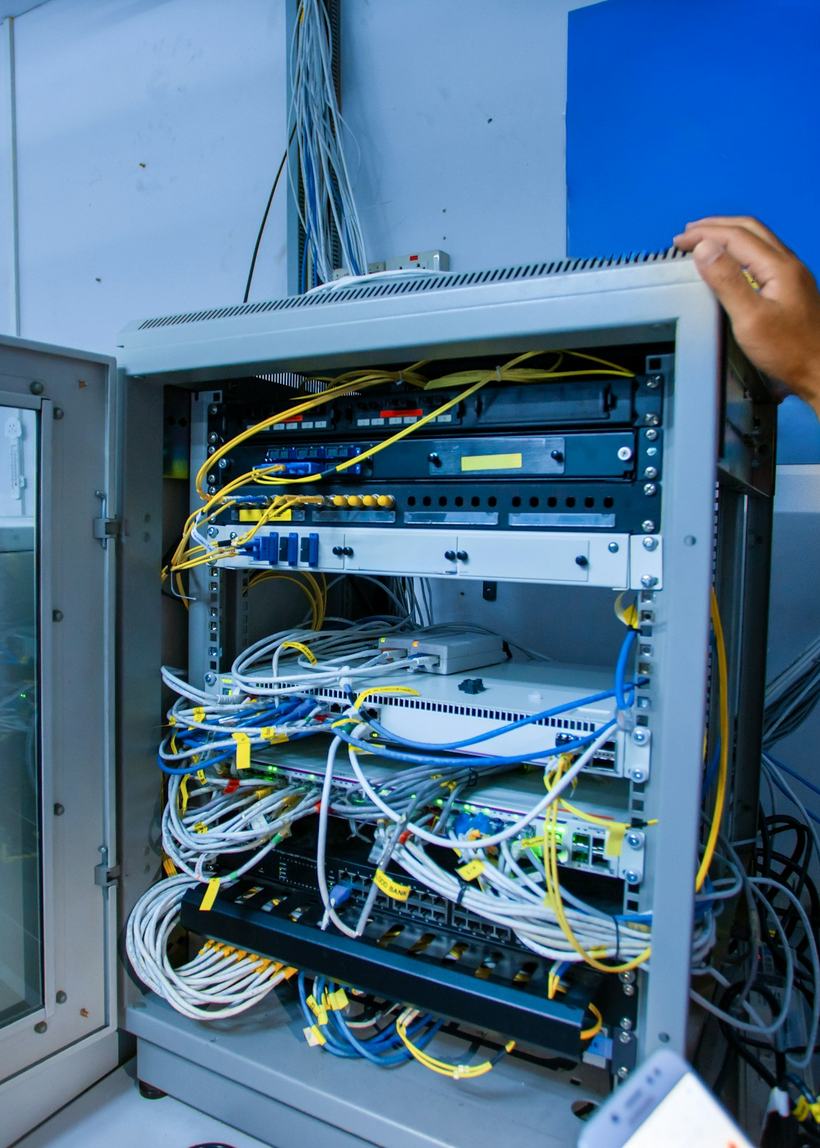 A technician opening a wall-mounted comms cabinet to reach the patch panels and switches inside.